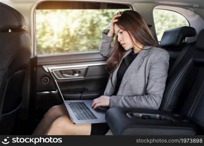 stressed young business woman using laptop computer while sitting in the back seat of car