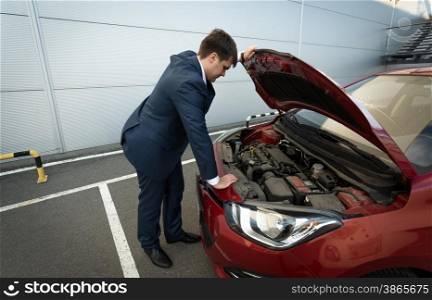 Stressed young businessman looking under the car hood