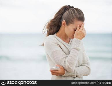 Stressed young woman in sweater on beach with cell phone