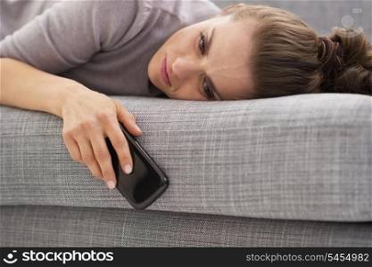 Stressed young woman with cell phone laying on couch