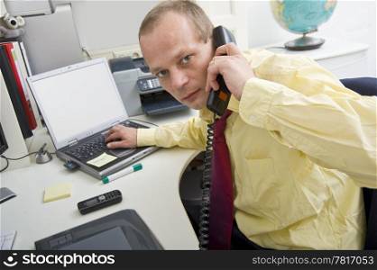 Stressful businessman making a telephone cal whilst typing on a laptop
