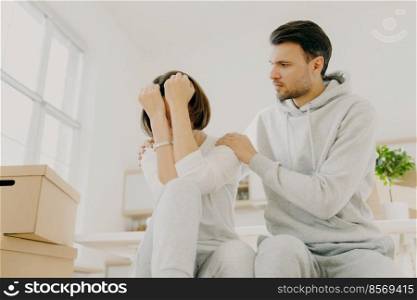 Stressful family couple forced to move home because of financial problems, woman complaining about someting, her affectionate husband tries to calm, pose indoor, carton filled containers around