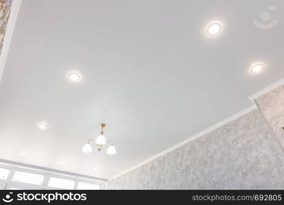 Stretch ceiling in the room with a chandelier and spotlights