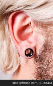 Stretched lobe piercing, grunge concept. Pierced man ear with black plug tunnel. Pierced man ear, black plug tunnel