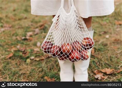 String bag with red apples. View of female legs in white boots walking through the autumn garden with eco bag in hands. Zero waste concept. No plastic life. Healthy fitness lifestyle. Recycling waste.. String bag with red apples. View of female legs in white boots walking through the autumn garden with eco bag in hands. Zero waste concept. No plastic life. Healthy fitness lifestyle. Recycling waste