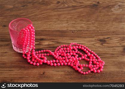 Strings of pink beads displayed in a fancy glass vase on a wooden background