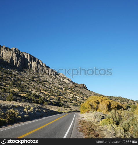 Strip of highway cutting through montain range under clear blue sky.