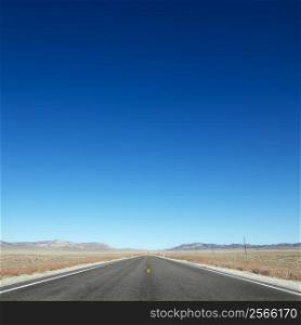 Strip of highway stretching towards horizon under clear blue sky.