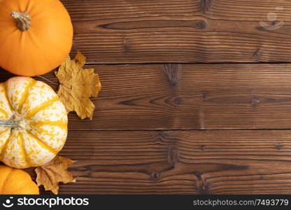 Striped yellow and orange pumpkins and dry maple autumn leaves on wooden background, top view, Halloween concept. Pumpkins and autumn leaves