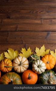 Striped yellow and orange pumpkins and dry maple autumn leaves on wooden background, top view, Halloween concept. Pumpkins and autumn leaves