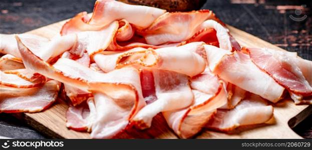 Strips of bacon on a cutting board. Against a dark background. High quality photo. Strips of bacon on a cutting board.
