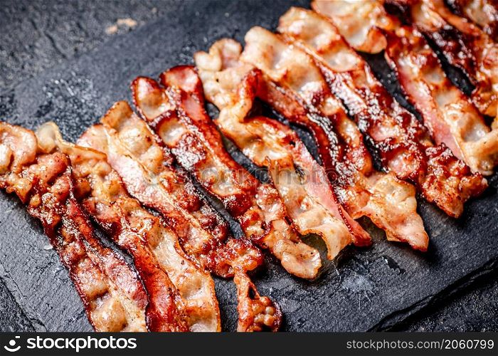 Strips of fried bacon on a black background. High quality photo. Strips of fried bacon on a black background.
