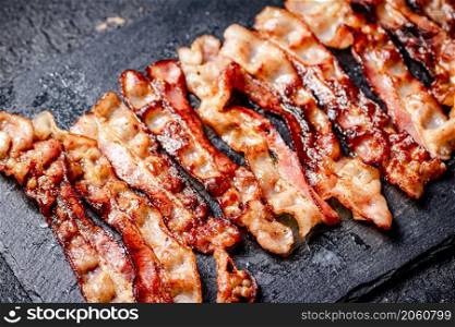 Strips of fried bacon on a black background. High quality photo. Strips of fried bacon on a black background.
