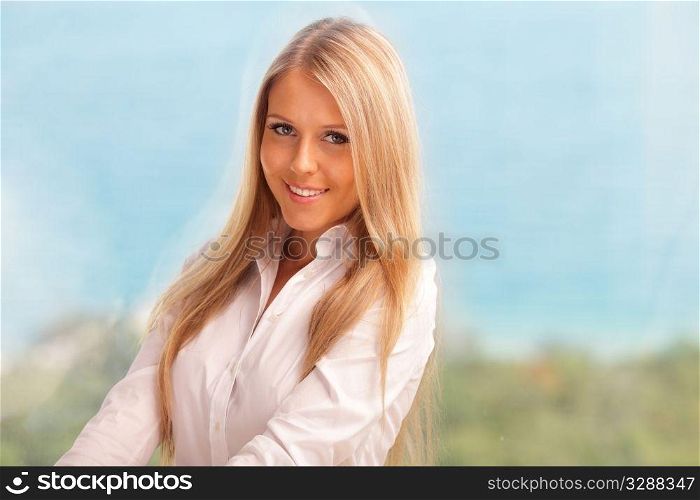 Strkingly beautiful woman with a happy smile sitting at home. Seaview in the background