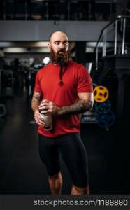 Strong athlete drinks water after exercise with dumbbells, workout in gym. Bearded sportsman on training in sport club, healthy lifestyle. Strong athlete drinks water, workout in gym