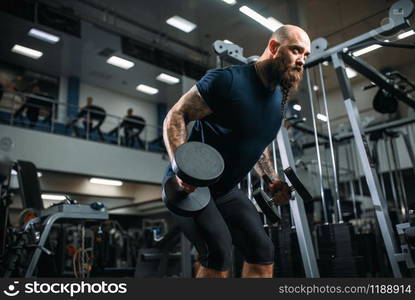 Strong athlete with dumbbells, training in gym. Bearded sportsman on workout in sport club. Strong athlete with dumbbells, training in gym