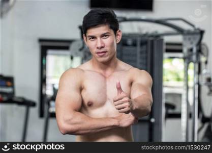 Strong Athletic Asian Man standing with crossed arms and looking at camera on gym showing thumbs up for good health,Muscular guy feeling so strong and healthy,Bodybuilder Concept