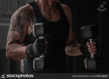 Strong bodybuilder, power athletic man in training pumping up muscles with dumbbell in gym or fitness club.