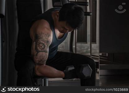 Strong bodybuilder, power athletic man in training pumping up muscles with dumbbell in gym or fitness club.