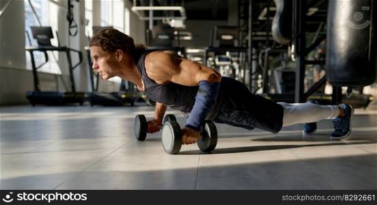 Strong bodybuilder with muscular body doing push-up with dumbbells at training gym. Sport and motivation concept. Strong bodybuilder with muscular body doing push-up with dumbbells