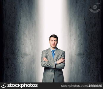 Strong enought to resist. Young confident businessman with hands crossed on chest between two walls