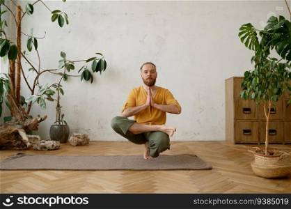 Strong fit man balancing on one leg in squatting position. Young male athlete exercising Ardha Padma Padangushthasana yoga pose. Strong fit man balancing on one leg in squatting position