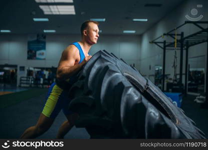 Strong male athlete doing strength exercise with truck tyre in gym, crossfit workout. Cross fit training in fitness club. Athlete doing exercise with truck tyre, crossfit