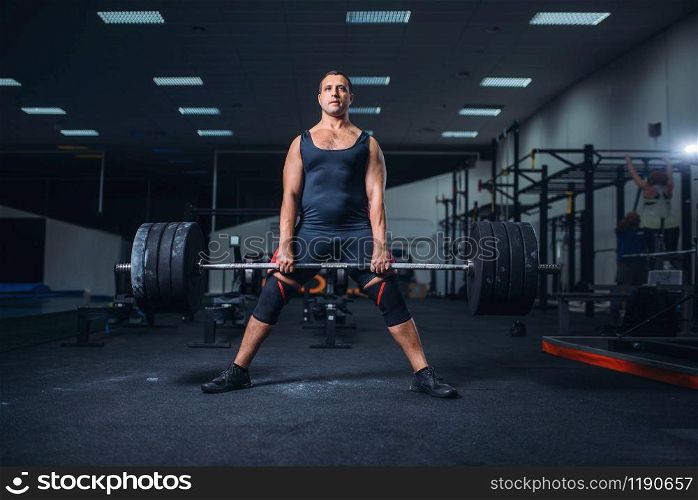 Strong male powerlifter keeps the weight of heavy barbell in gym. Weightlifting workout, lifting training, muscular athlete in sport club. Powerlifter keeps the weight of heavy barbell