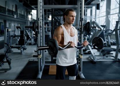 Strong man athlete training muscles with barbell during physical workout in sport gym. Bodybuilder pumping up biceps lifting weights practicing functional exercises. Man athlete training muscles with barbell during physical workout in sport gym