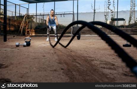 Strong man doing exercise with ropes, street workout, crossfit. Fitness training on sports ground outdoor, male person pumps muscles, active urban lifestyle. Man doing exercise with ropes, workout, crossfit