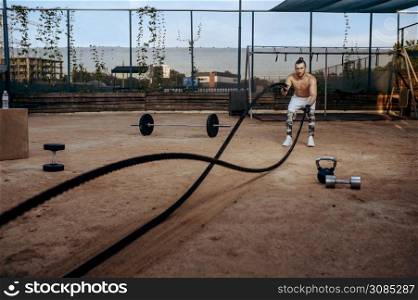 Strong man doing exercise with ropes, street workout, crossfit. Fitness training on sports ground outdoor, male person pumps muscles. Man doing exercise with ropes, workout, crossfit
