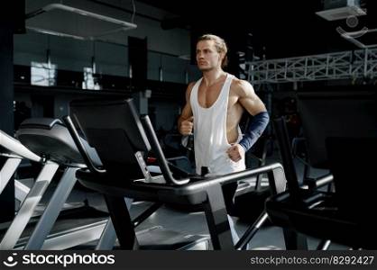 Strong muscular man running on treadmill at modern sport gym. Athletic male bodybuilder jogging on stationary machine doing cardio training. Strong muscular man running on treadmill at modern sport gym