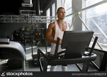 Strong muscular man running on treadmill at modern sport gym. Athletic male bodybuilder jogging on stationary machine. Strong muscular man running on treadmill at modern sport gym
