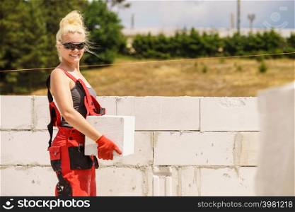 Strong pretty woman working on construction site, building house, installing gray airbricks. Industrial work concept.. Woman working with airbricks