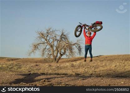 strong senior male cyclist is lifting a fat mountain bike when biking in northern Colorado prairie, early spring scenery in Soapstone Prairie Natural Area near Fort Collins