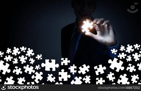 Strong solution finding ability. Businesserson on dark background taking puzzle element with fingers