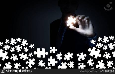 Strong solution finding ability. Businesserson on dark background taking puzzle element with fingers