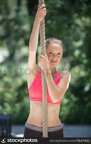 strong sportswoman climbing rope in the park