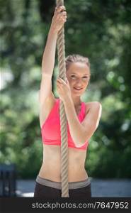 strong sportswoman climbing rope in the park