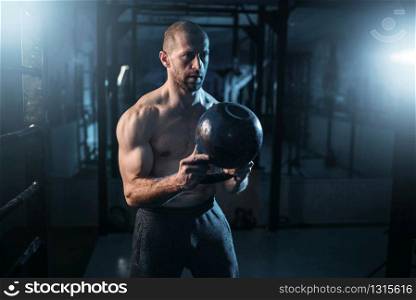 Strong weightlifter workout with kettlebell in gym. Man with muscular torso training with weight. Strong weightlifter workout with weight in gym