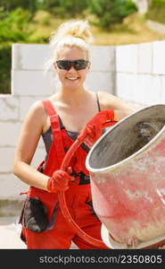 Strong woman worker working with red concrete cement mixer machine on house construction site. Industrial work equipment concept.. Strong woman working with construction site