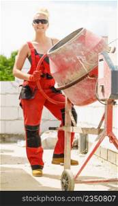 Strong woman worker working with red concrete cement mixer machine on house construction site. Industrial work equipment concept.. Strong woman working with construction site