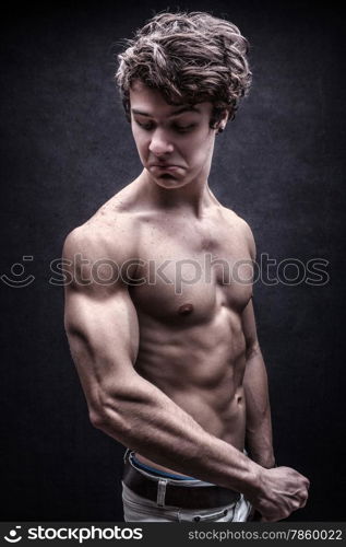 Strong young man looked down dissatisfied to his arm muscles