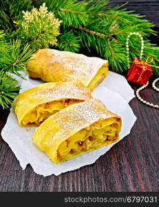 Strudel pumpkin and apple with raisins on paper, pine branches with Christmas toys in the background of a wooden board