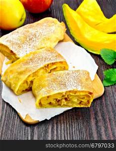 Strudel pumpkin and apple with raisins on parchment, fruits and vegetables on a dark wooden board