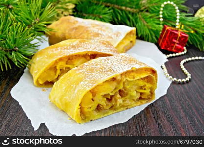 Strudel pumpkin and apple with raisins on parchment, pine branches with Christmas toys in the background of a wooden board