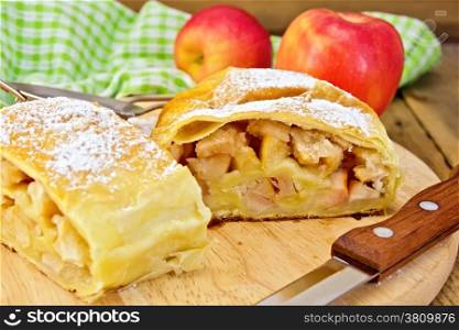 Strudel with apples, apples, a knife, a strainer, a napkin on the background of wooden boards