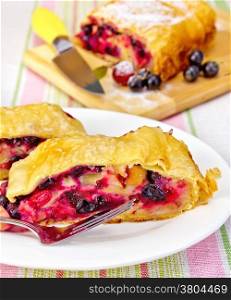 Strudel with black currant and cherry on a plate with fork, knife on background linen tablecloth