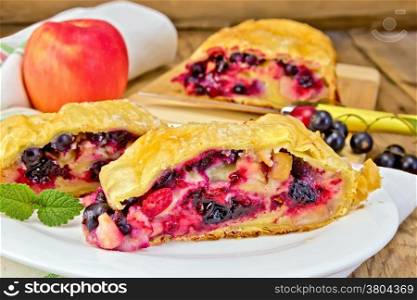 Strudel with black currant, apple and cherry on a plate, napkin, apple on the background of wooden boards