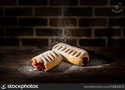 Strudel with cherries powdered with sugar on a wooden table and brick background